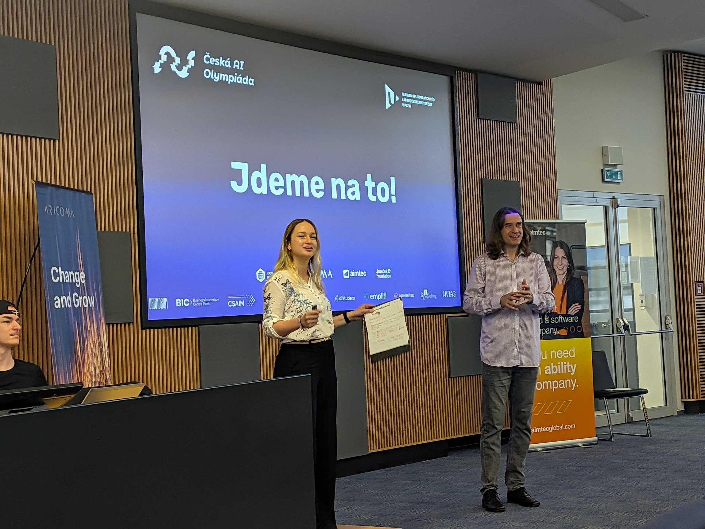 Two speakers in front of a Czech AI Olympiad projection at the Faculty of Applied Sciences